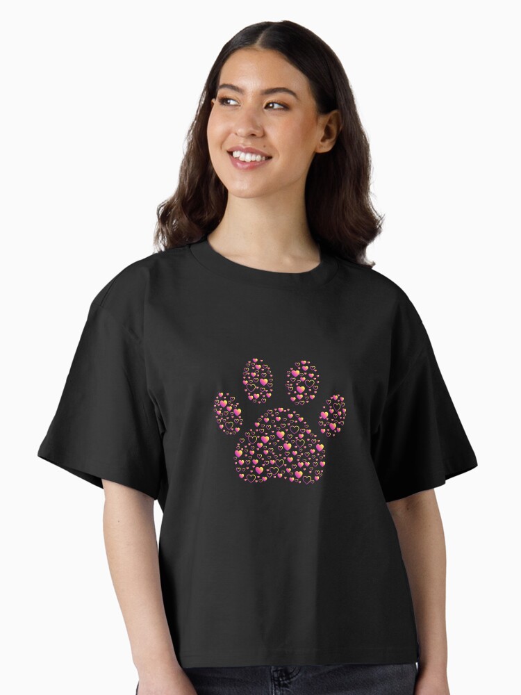 Photo of a person wearing a black t-shirt with a paw print on the chest made up of different sized hearts in a pink to yellow gradient.